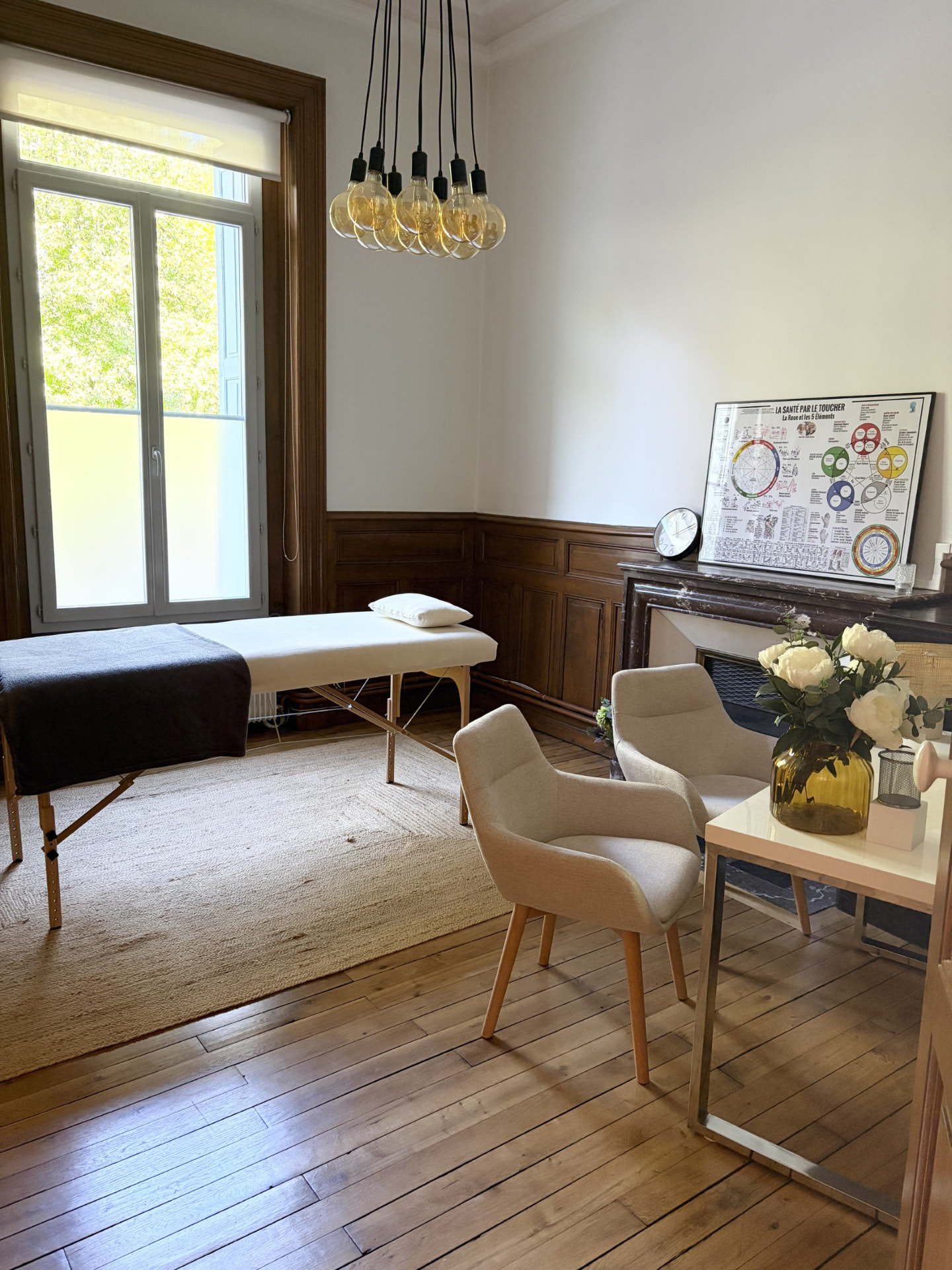 Cabinet de kinésiologie au Puy-en-Velay : table de soin près de la fenêtre, fauteuils et affiche La santé par le toucher